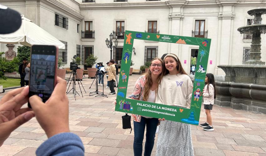 Fotografía de una mujer y una niña, muy sonrientes, con el Patio de los Naranjos del Palacio de La Moneda de fondo. Fotografía tomada el Día  de los Patrimonios.